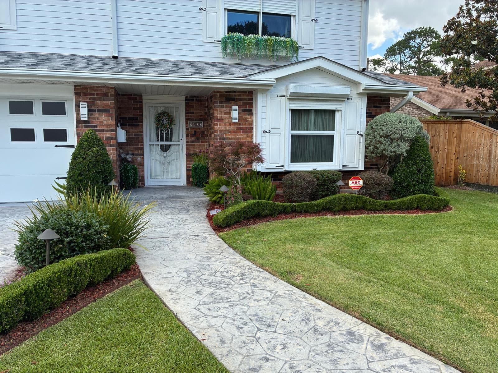 Front of a Greater New Orleans home with trimmed hedges, fresh beds and a stamped concrete walkway by KoKo Construction